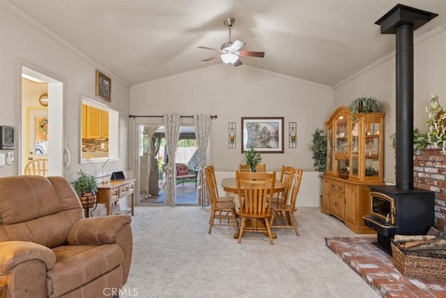 carpeted dining space featuring a wood stove, ceiling fan, vaulted ceiling, and ornamental molding