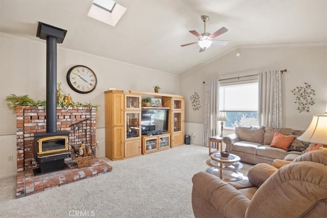 carpeted living room featuring ceiling fan, a wood stove, ornamental molding, and lofted ceiling with skylight