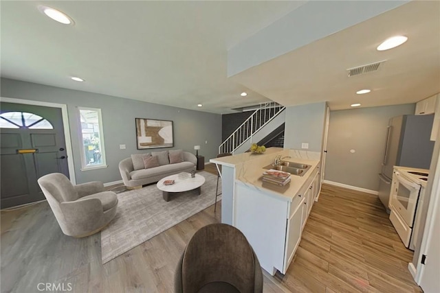 kitchen featuring kitchen peninsula, sink, white electric stove, light hardwood / wood-style floors, and white cabinetry