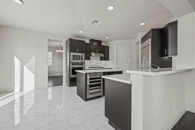 kitchen with kitchen peninsula, beverage cooler, built in appliances, a notable chandelier, and a kitchen island