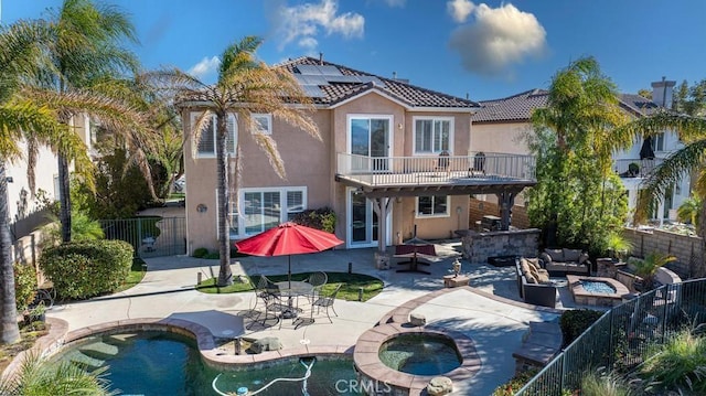 rear view of house featuring solar panels, a balcony, an outdoor living space with a fire pit, a pool with hot tub, and a patio area