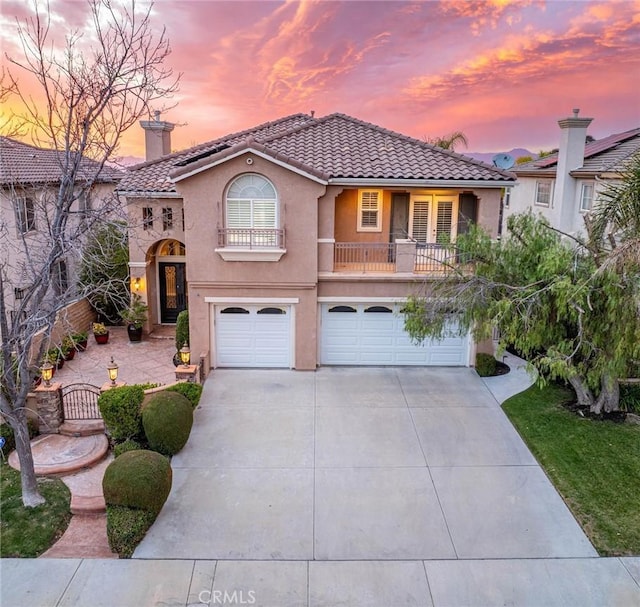 mediterranean / spanish house featuring a garage, concrete driveway, a balcony, a tiled roof, and stucco siding