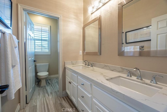 full bathroom featuring toilet, double vanity, baseboards, and a sink