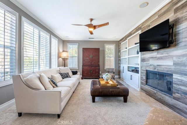 carpeted living room with built in features, a fireplace, ornamental molding, a ceiling fan, and baseboards