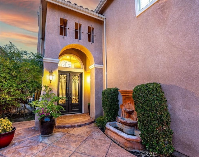 exterior entry at dusk featuring stucco siding and french doors