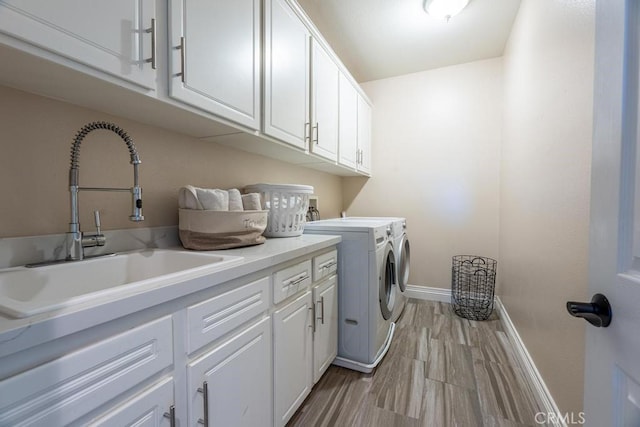 clothes washing area featuring cabinet space, light wood-style floors, a sink, separate washer and dryer, and baseboards