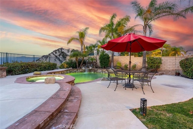 patio terrace at dusk with a fenced backyard and an in ground hot tub