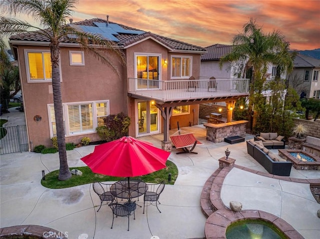 back of house at dusk with solar panels, stucco siding, an outdoor living space with a fireplace, a patio area, and a tiled roof