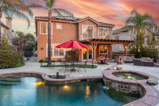 back of property at dusk with solar panels, a patio, an outdoor hangout area, fence, and stucco siding