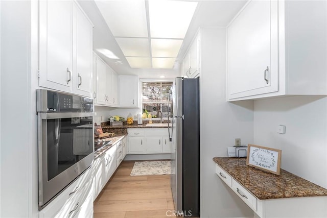 kitchen featuring sink, stainless steel fridge, dark stone countertops, light wood-type flooring, and white cabinetry