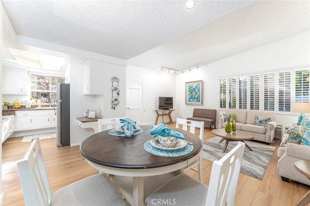 dining space featuring a textured ceiling, light hardwood / wood-style flooring, and lofted ceiling