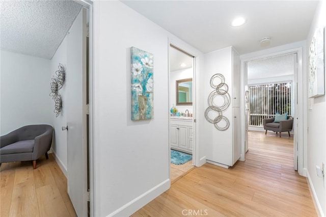 hallway with a textured ceiling, light hardwood / wood-style flooring, and sink