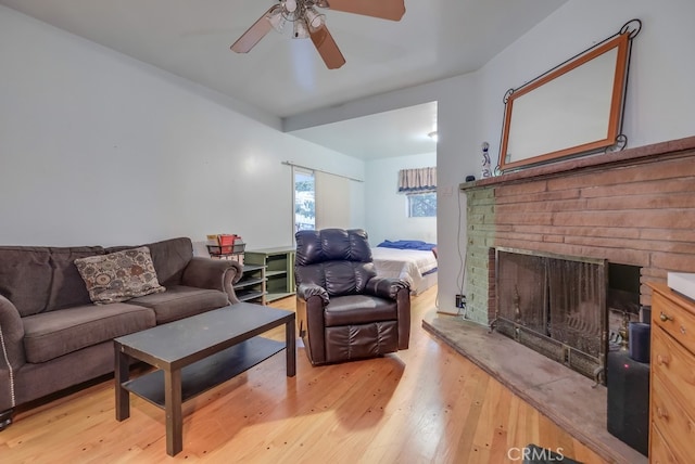 living room with light wood-type flooring, ceiling fan, and a fireplace