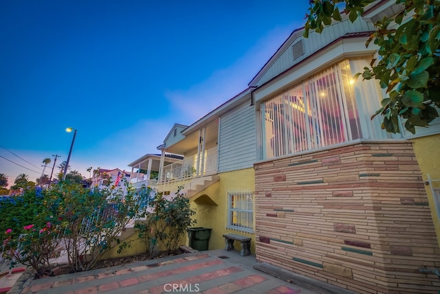 property exterior at dusk featuring a balcony and a patio area