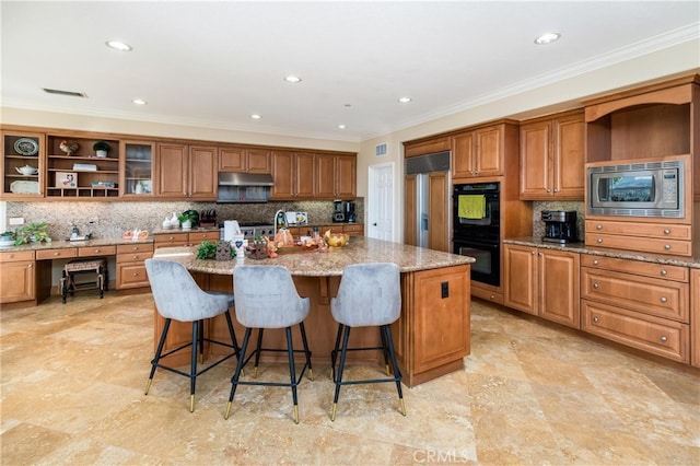 kitchen with tasteful backsplash, light stone counters, a kitchen island with sink, built in appliances, and a breakfast bar area