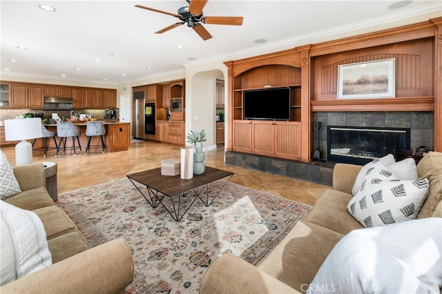 living room with a tile fireplace, ceiling fan, and crown molding