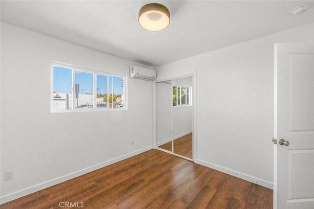 unfurnished bedroom featuring dark hardwood / wood-style floors, an AC wall unit, and a closet