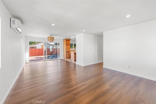 unfurnished living room featuring dark hardwood / wood-style floors, an AC wall unit, and a healthy amount of sunlight