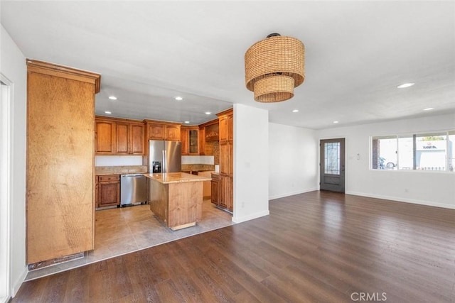 kitchen featuring appliances with stainless steel finishes, light stone countertops, a kitchen island, and light wood-type flooring