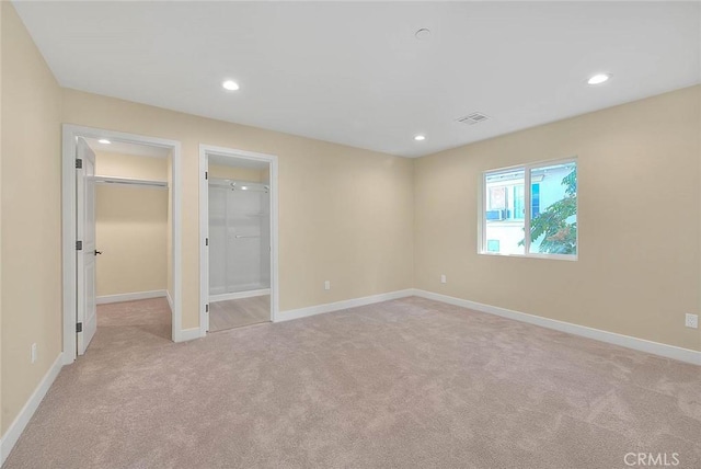 unfurnished bedroom featuring light carpet, a walk in closet, and a closet