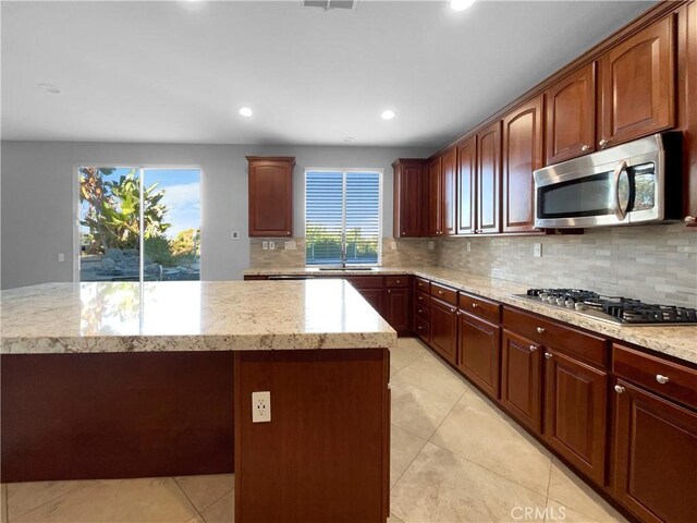 kitchen featuring decorative backsplash, appliances with stainless steel finishes, sink, light tile patterned floors, and a kitchen island