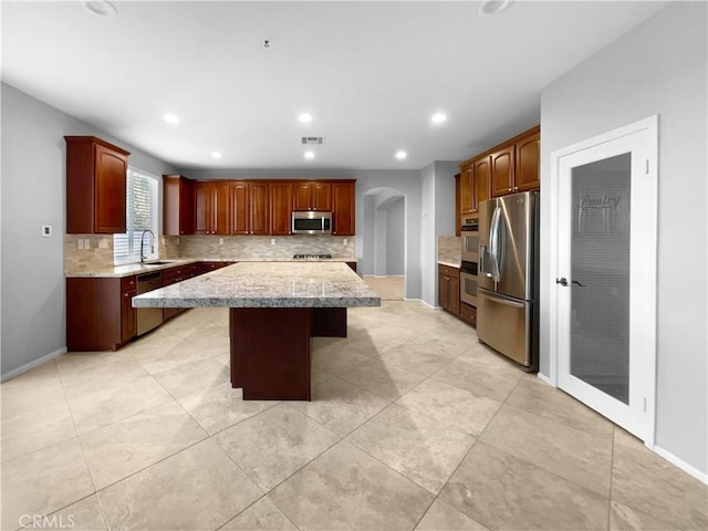 kitchen with sink, decorative backsplash, appliances with stainless steel finishes, a kitchen island, and a kitchen bar