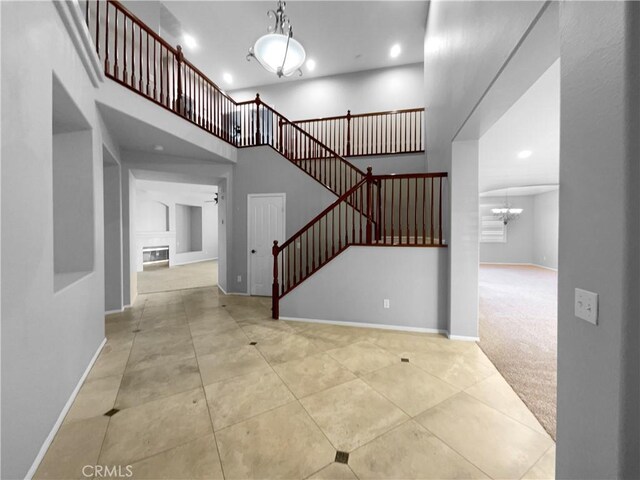 entrance foyer featuring ceiling fan with notable chandelier, light carpet, and a towering ceiling