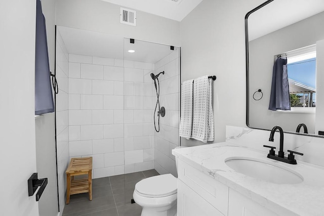 bathroom featuring toilet, a tile shower, vanity, and tile patterned floors