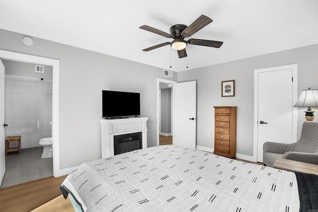 bedroom featuring ceiling fan, light wood-type flooring, tile walls, and ensuite bath