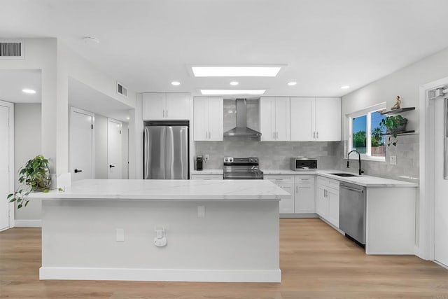 kitchen with white cabinets, wall chimney exhaust hood, sink, and stainless steel appliances