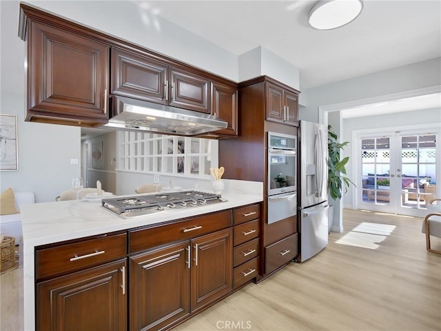 kitchen featuring light stone countertops, french doors, stainless steel appliances, light hardwood / wood-style floors, and dark brown cabinets