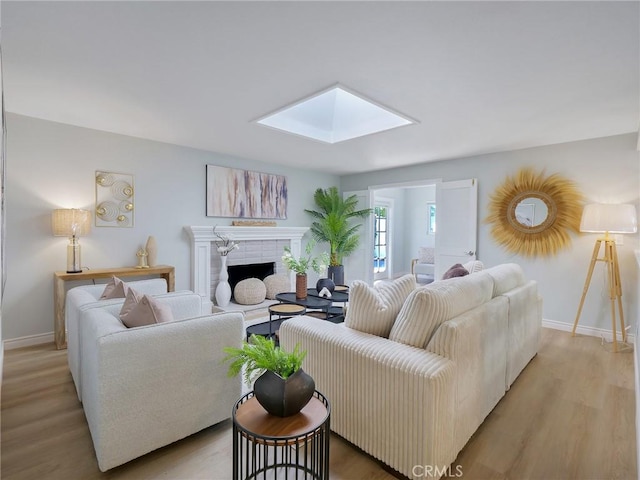 living room featuring a brick fireplace, light wood-type flooring, and a skylight