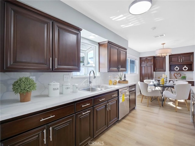 kitchen with pendant lighting, backsplash, sink, stainless steel dishwasher, and light wood-type flooring