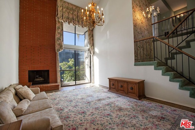 living room featuring hardwood / wood-style floors, a towering ceiling, a chandelier, and a brick fireplace