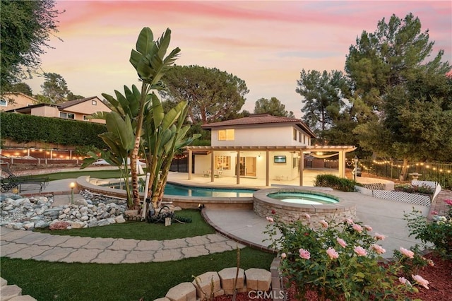 back house at dusk with a swimming pool with hot tub, a pergola, and a patio area