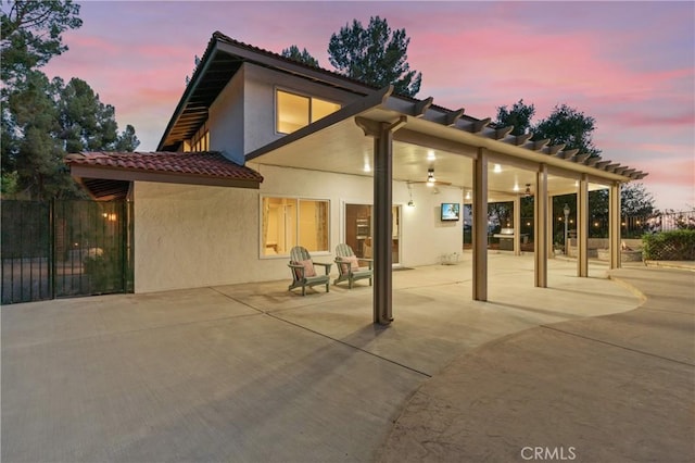 back house at dusk featuring ceiling fan and a patio area