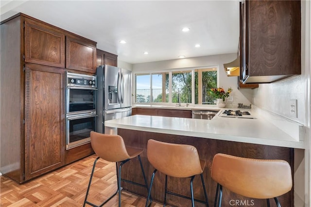 kitchen with a breakfast bar, sink, appliances with stainless steel finishes, kitchen peninsula, and light parquet flooring