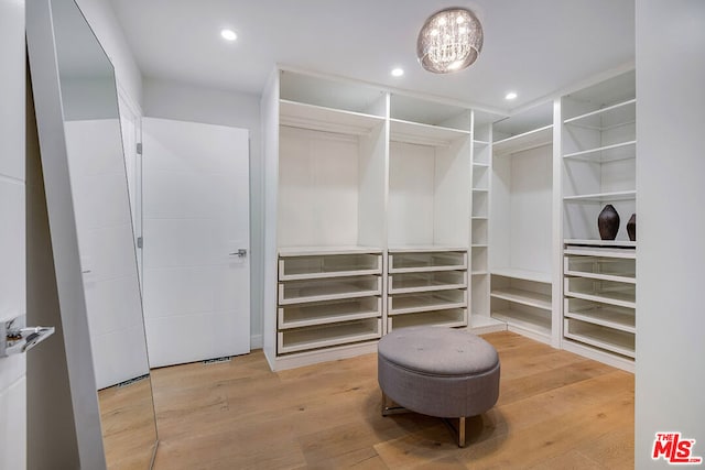 spacious closet with light hardwood / wood-style flooring and a chandelier