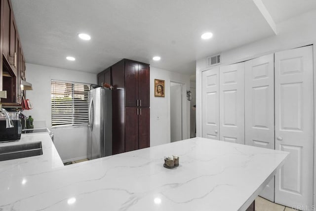 kitchen with visible vents, light stone counters, freestanding refrigerator, a peninsula, and recessed lighting