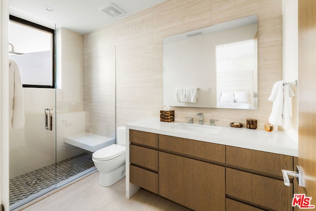 bathroom featuring walk in shower, vanity, toilet, and tile walls