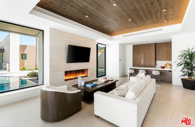 living room featuring a large fireplace, a raised ceiling, and wood ceiling