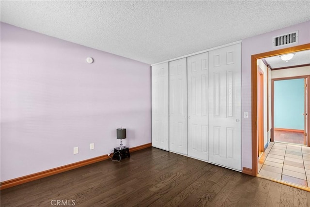 unfurnished bedroom with dark wood-type flooring, a textured ceiling, and a closet