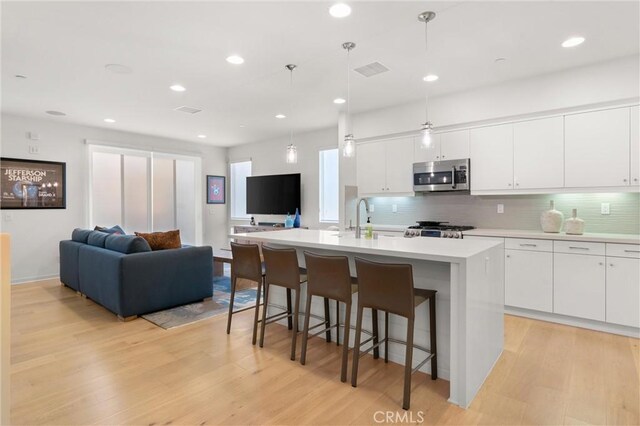 kitchen with appliances with stainless steel finishes, pendant lighting, light hardwood / wood-style floors, and a center island with sink