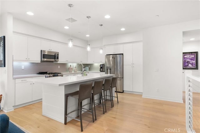 kitchen with white cabinets, light hardwood / wood-style floors, a kitchen island with sink, and appliances with stainless steel finishes