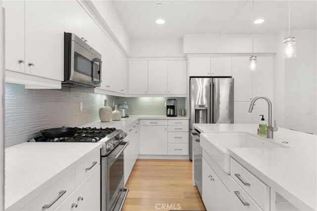 kitchen with white cabinetry, light hardwood / wood-style flooring, hanging light fixtures, and appliances with stainless steel finishes