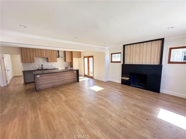 unfurnished living room featuring sink, light hardwood / wood-style flooring, a healthy amount of sunlight, and ornamental molding