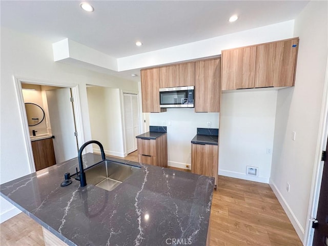 kitchen featuring dark stone countertops, sink, and light wood-type flooring