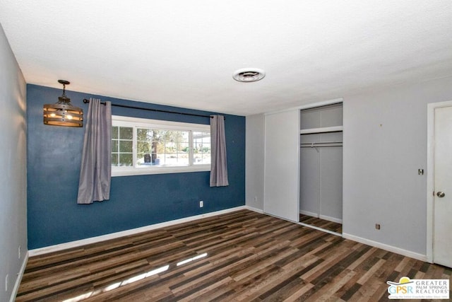 unfurnished bedroom with a textured ceiling, dark wood-type flooring, and a closet