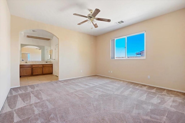 unfurnished bedroom with sink, light colored carpet, ceiling fan, and ensuite bathroom