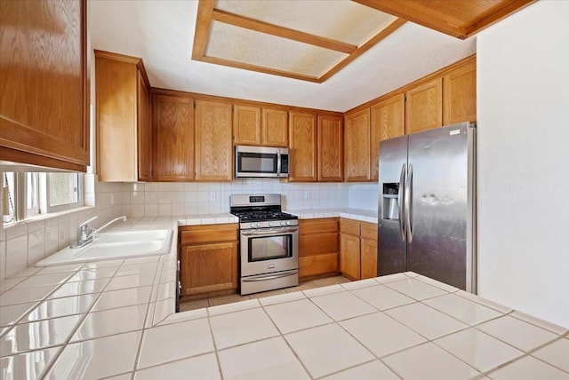 kitchen with appliances with stainless steel finishes, tasteful backsplash, tile counters, and sink